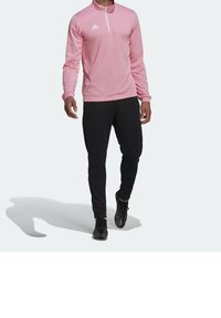 Ljusrosa långärmad träningströja med dragkedja vid halsen och elastiska ärmslut, tillsammans med svarta figurnära byxor och svarta träningenskor.