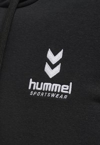 Černá mikina s kapucí vyrobená z měkké tkaniny, zdobená bílým vyšitým logem se dvěma chevronovými vzory a textem "hummel SPORTSWEAR."