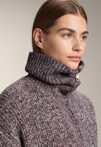 Pletený sveter z viacfarebnej priadze s vysokým rebrovaným golierom a zipsom. Má štruktúrovaný vzor v odtieňoch fialovej a smotanovej.