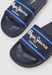 Chanclas de slide en color navy con rayas azules y un logotipo en relieve en blanco que dice "Pepe Jeans London". Hechas de un material sintético liso y texturizado.