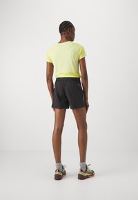 Camiseta deportiva amarilla de manga corta combinada con pantalones cortos negros. Presenta un corte relajado, tejido suave y un diseño minimalista. Zapatillas negras con calcetines grises.