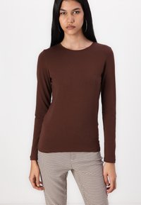 Bluza maro cu mânecă lungă, decolteu rotund, design ajustat și textură netedă. Asortată cu pantaloni cu un model în carouri.