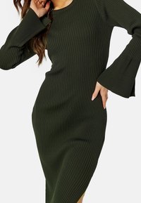 Robe en tricot côtelé de couleur vert foncé, avec manches longues évasées et coupe mi-longue, dotée d'un col rond et d'une silhouette ajustée.