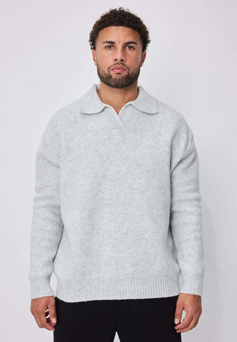 Pull en maille gris clair avec un col classique, des manches longues et un ourlet côtelé. Texture douce avec une coupe légèrement ample.