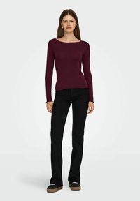 Bordeaux lange mouwen top met een bootnek, gecombineerd met zwarte uitlopende broek en donkere instappers. Eenvoudig ontwerp, zachte textuur.