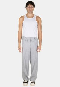 Pantaloni grigi a gamba larga con chiusura a bottone e tasche laterali, abbinati a un top bianco senza maniche e sneaker bicolore. Tessuto dalla superficie liscia.