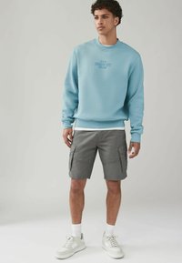 Svetlo modrý bavlnený sweatshirt s okrúhlym výstrihom a prednou grafikou, skombinovaný s šedými cargo šortkami s viacerými vreckami a voľným strihom.
