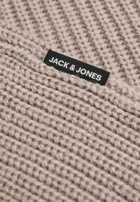 Strickstoff in Hellbeige mit strukturiertem Muster. Verfügt über ein schwarzes Etikett mit weißem Text "JACK & JONES", das deutlich sichtbar ist.