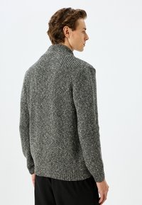 Grauer gerippter Strickpullover mit hohem Kragen, mit einer strukturierten Oberfläche und eng anliegenden Bündchen, entworfen für einen lässigen Schnitt.