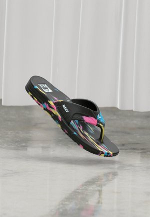 Schwarze Flip-Flop-Sandale von Black Reef mit bunten gelben, pinken und blauen Streifen auf Riemen und Sohle, schwebend über einem grauen polierten Boden.