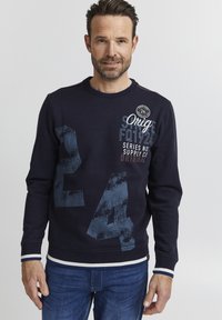 Námornícky sveter s veľkým, vyblednutým modrým číslom "24" a logom. Okrúhly výstrih, rebrované manžety a spodný lem s bielymi a modrými pásikmi.