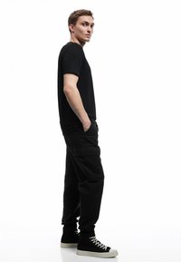 Czarny bawełniany t-shirt w połączeniu z czarnymi spodniami cargo i sneakersami typu high-top. Charakterystyczne cechy to boczne kieszenie i luźny krój.