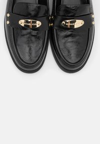 Paire de mocassins en cuir noir brillant avec plaques métalliques dorées Michael Kors et clous décoratifs dorés sur le dessus.