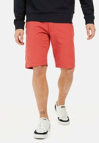 Røde shorts lavet af letvægtsstof, midt på låret, med flad front, sidelommer og båret med hvide sneakers med marineblå accenter.