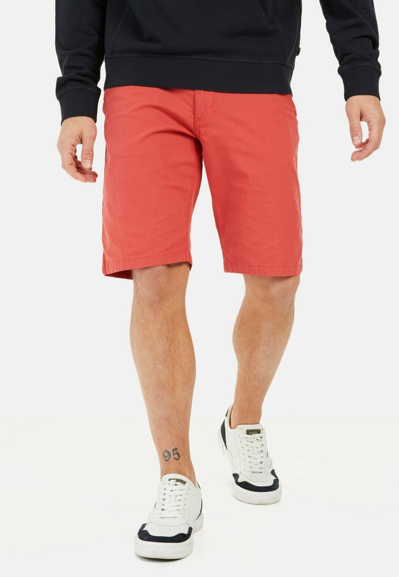Røde shorts lavet af letvægtsstof, midt på låret, med flad front, sidelommer og båret med hvide sneakers med marineblå accenter.