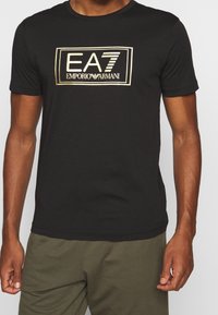 Svart bomull t-shirt med en gul EA7 Emporio Armani-logotyp centrerad på framsidan, korta ärmar och rund halsringning.