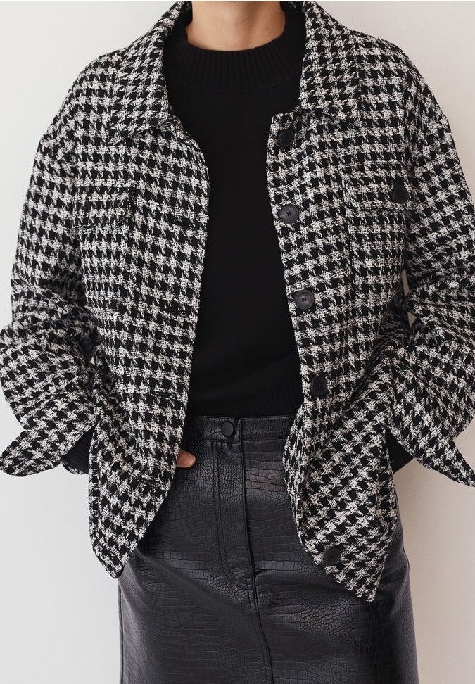 Veste pied-de-poule en noir et blanc avec col, boutons à l'avant et deux poches poitrine, associée à une jupe noire texturée.