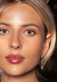 Zilveren druppeloorbellen met een slank, langwerpig ontwerp hangen aan het oor van een model en complementeren haar natuurlijke make-up en lichte blonde haar.