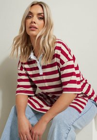 Rot-beige gestreiftes Polohemd mit einem weißen Kragen. Kurzärmlig, lockere Passform. Getragen mit hellblauen, weit geschnittenen Jeans.