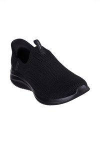 Zapatilla deportiva negra sin cordones con parte superior de punto transpirable, diseño texturizado y suela de goma flexible. Cuenta con un lazo para facilitar el uso.