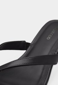 Μαύρο δερμάτινο σανδάλι με λεπτούς, διασταυρωμένους ιμάντες και αναπαυτική σόλα, εμφανιζόμενο σε κοντινή εικόνα με απλό φόντο.