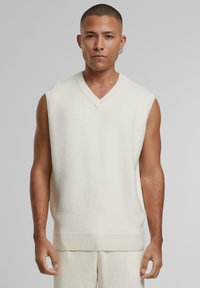 Pulover din tricot fără mâneci, de culoare fildeș, cu decolteu în V, bordură cu nervuri și textură moale, conceput pentru o croială lejeră, având slituri laterale.