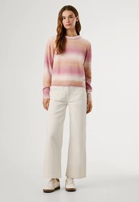 Camisola de malha com padrão em gradiente de riscas cor-de-rosa e creme, combinada com calças largas brancas e ténis creme. Textura suave, corte casual.