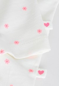 Tissu blanc avec de petites fleurs roses et des bords cousus, avec des onglets blancs ornés de motifs de cœurs roses sur les côtés.