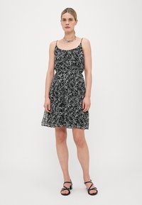 Vestido negro con flores, tirantes finos, cintura ajustada y falda acampanada. El material parece ligero y tiene una textura suave. Se lleva con sandalias negras.
