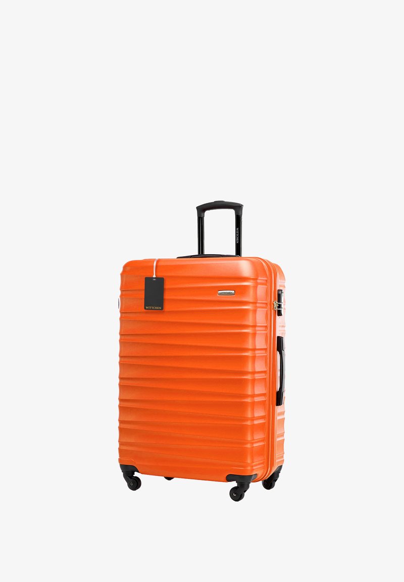 Valise rigide orange avec des rainures verticales, poignée télescopique noire, poignée latérale et quatre roues pivotantes. Étiquette attachée à la poignée.