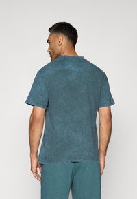 Kortærmet, rundhalset t-shirt i en falmet blå farve, med en tekstureret overflade og afslappet pasform, vist fra bagsiden.