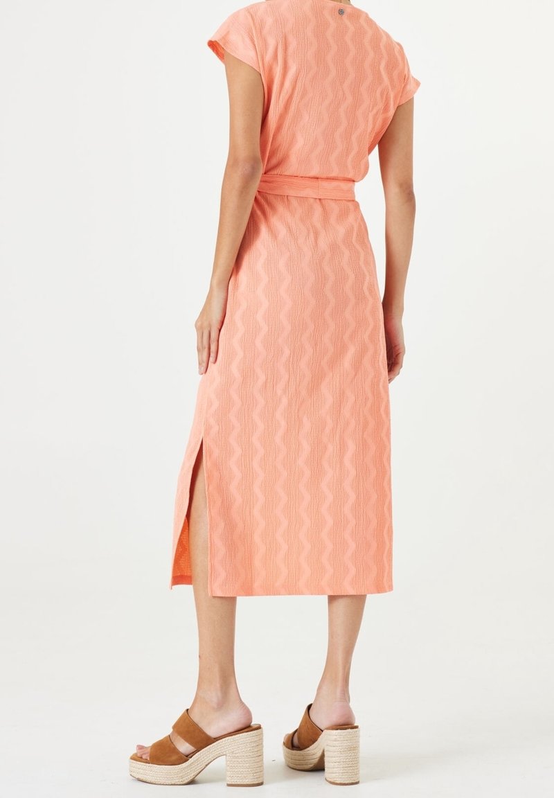Robe midi couleur pêche avec une texture ondulée, manches courtes et une fente latérale, associée à des sandales à talons blocs marron avec brides.