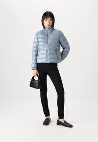 Lyseblå pufferjakke med høy krage, glidelås foran og quiltet mønster; kombinert med svarte skinny jeans og svarte loafers.