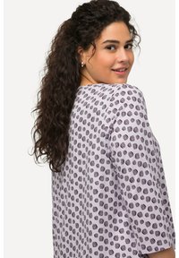 Top de color púrpura claro con patrones circulares negros, corte relajado, mangas de tres cuartos, escote redondo y textura de tela suave.