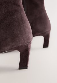 Suede ankle boots in dark purple with a curved heel. The texture is soft, and the design features a side zipper for easy wear.