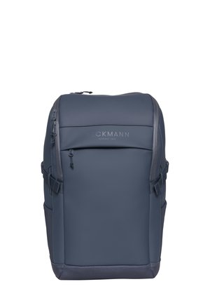 Mørkegrå rektangulær ryggsekk med glidelåslomme foran og stropp på siden, står oppreist på hvit bakgrunn.