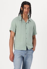 Lichtgroen kortom shirt met knopen in een gestructureerde stof, met een kraag, knopen aan de voorkant en een relaxte fit, gecombineerd met een blauwe spijkerbroek.