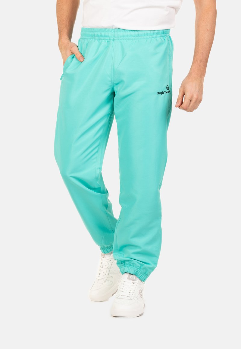 Turquoise sportbroek met een elastische tailleband, zijzakken en elastische boorden. Bevat een logo op de linkerdij. Gladde textuur.
