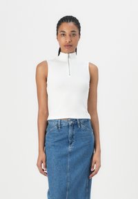 Vit ärmlös topp med hög krage och silverfärgad dragkedja, kombinerad med en högmidjad blå denimkjol. Slät textur, skräddarsydd design.