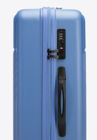 Hard-shell suitcase in light blue, featuring a textured surface, black zipper, combination lock, and a side handle for easy transport.