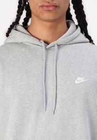 Sweatshirt cinzenta mesclada em tecido macio, com capuz ajustável por cordão e pequeno logótipo branco da Nike no peito. Textura suave.