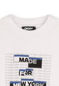 T-shirt en coton blanc avec un design graphique et le texte "FAIT POUR NEW YORK" en bleu et noir, sur un fond à motifs.
