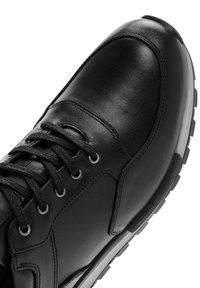 Sneaker in pelle nera con lacci neri, occhielli in metallo e suola in gomma con battistrada testurizzato, mostrato da un'angolazione ravvicinata dall'alto.