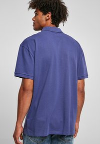 Polo-shirt violet foncé avec une texture douce. Présente un col classique et des manches courtes. Ourlet droit avec fentes latérales, porté avec un denim clair.