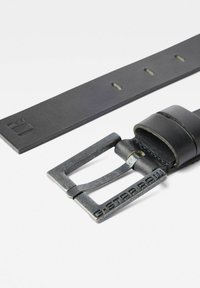 Cinturón de cuero negro con un acabado texturizado, que presenta una hebilla de metal con "G-STARRAW" grabado y múltiples agujeros de ajuste.
