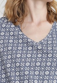 Top de manga corta en azul oscuro con patrones florales blancos; presenta un escote en V y una tela texturizada.