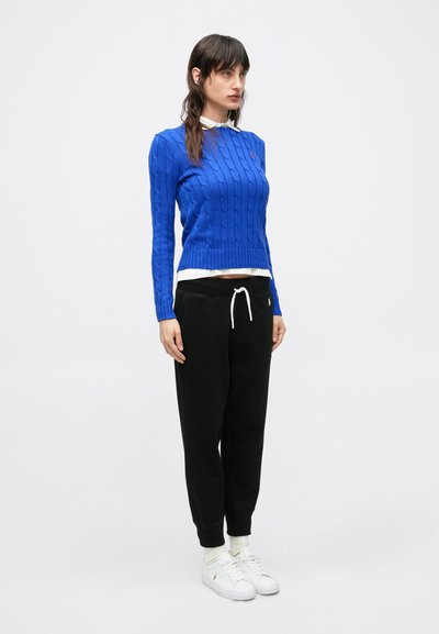 Kék, kötött mintás pulóver hosszú ujjakkal, fehér inggel rétegezve, fekete melegítőnadrággal és fehér tornacipővel párosítva. Egyszerű dizájn.