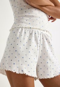 Vita stickade shorts med blå blommönster, med en volangkant och texturerade vertikala ränder. Elastisk midja för komfort.