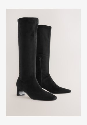 Zwarte suède laarzen tot aan de knie met een blokhak, puntige neus en details van een zijrits. Soepele textuur zonder zichtbare patronen of accenten.