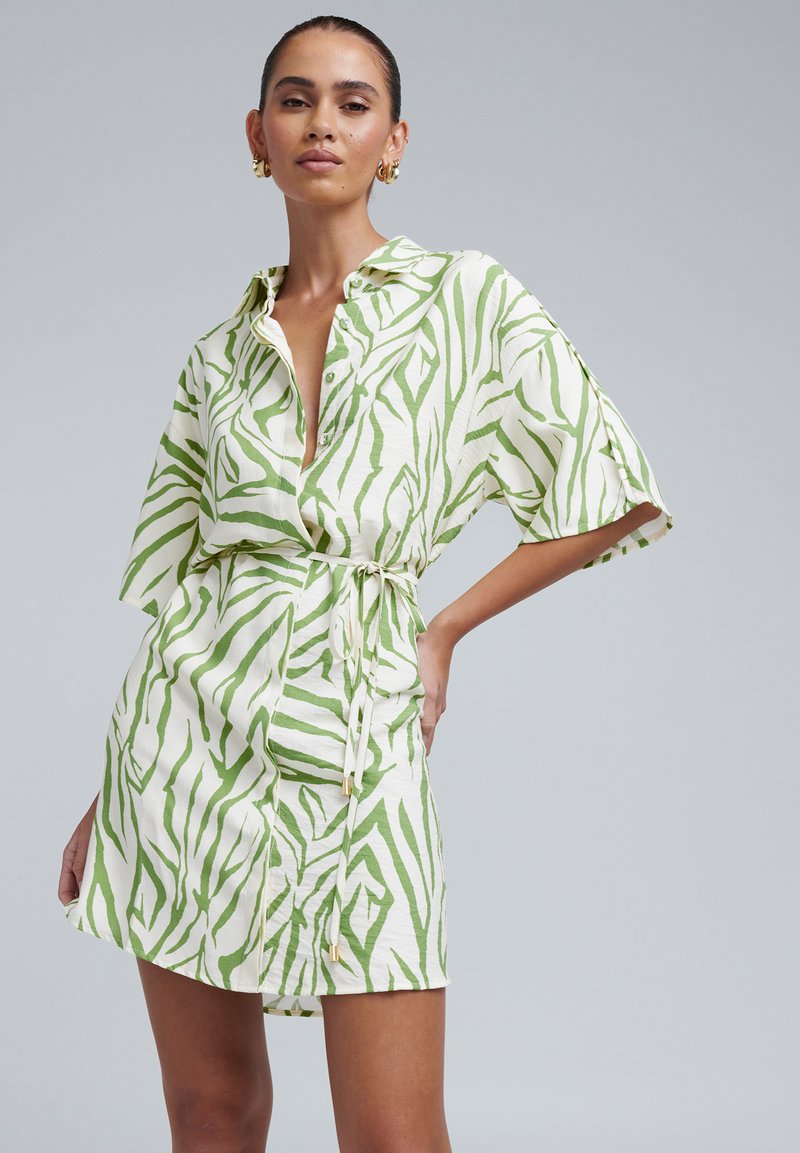 Kortærmet skjortekjole i hvid og grøn med zebrastribet mønster, bælte i taljen, knaplukning foran og en afslappet pasform.